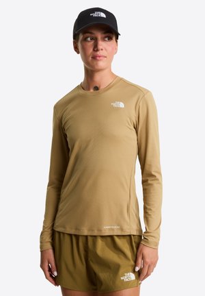 Camisa de manga larga, color marrón claro con un patrón texturizado, que presenta un escote redondo y un pequeño logotipo blanco en el pecho. Combinada con pantalones cortos de color verde oliva.