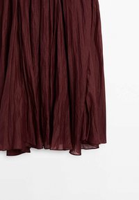 Jupe plissée rouge foncé en tissu léger semi-transparent avec une texture fluide légèrement froissée sur un fond uni.