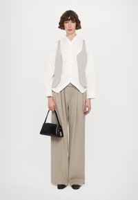 Camicia bianca con gilet grigio, ampi pantaloni beige e una piccola borsa nera. Tessuti morbidi e design su misura.