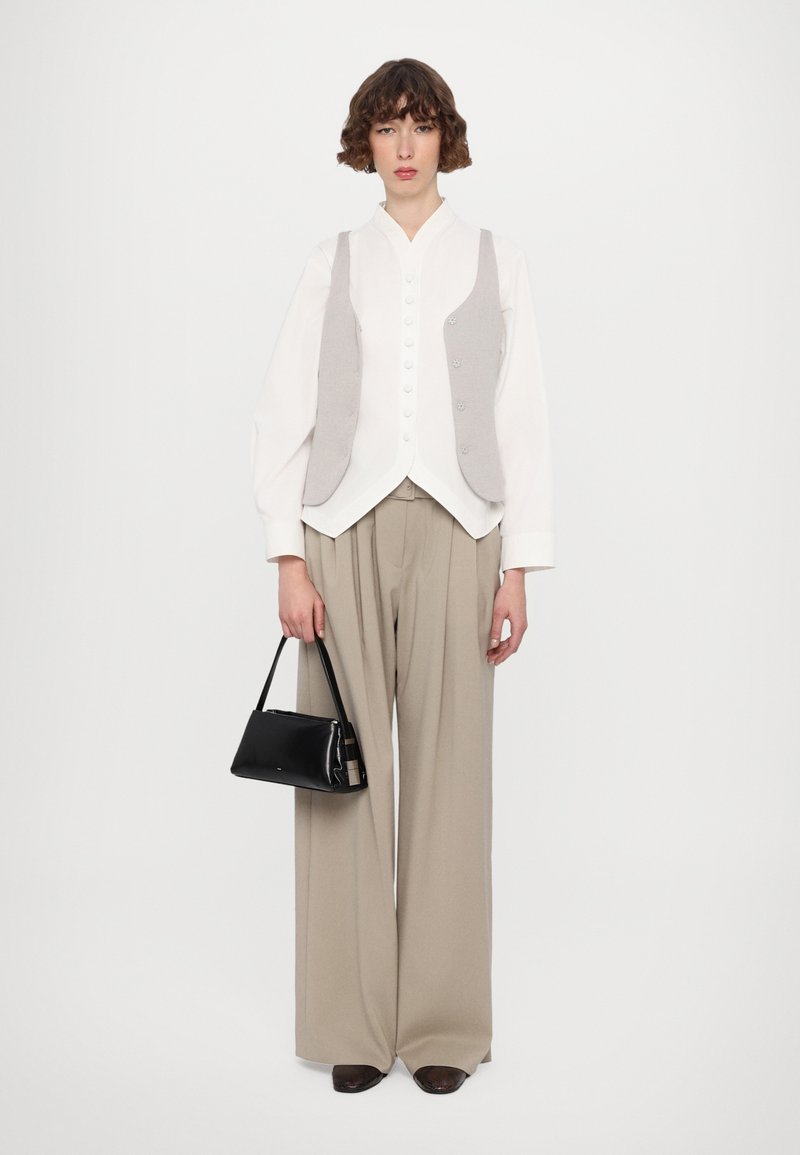 Camicia bianca con gilet grigio, ampi pantaloni beige e una piccola borsa nera. Tessuti morbidi e design su misura.