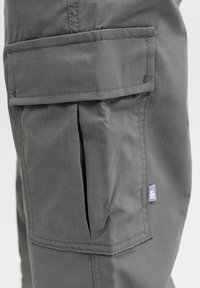 Sive cargo hlače s teksturiranom tkaninom. Imaju bočnu džepu s preklopom i šivenim detaljima, pružajući funkcionalnost i praktičnost.