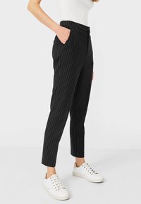 Zwarte pinstripe broek met taps toelopende benen en zijzakken, gemaakt van een gladde stof. Gecombineerd met witte sneakers voor contrast.