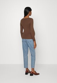Top castanho de mangas longas com decote redondo, combinado com jeans azuis claros de perna reta. Sapatos castanhos brilhantes com saltos quadrados.