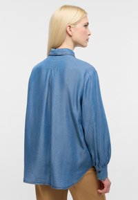 Helles blaues Denimhemd mit Kragen, langen Ärmeln und geknöpften Manschetten. Verfügt über eine Rückenfalte und einen abgerundeten Saum für eine lockere Passform.