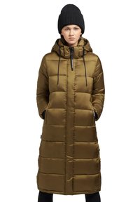 Long manteau rembourré olive vert avec capuche, comportant une fermeture éclair à l'avant, des cordons de serrage et des poches latérales. Porté avec un bonnet en tricot noir.
