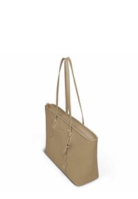 Sac fourre-tout en cuir beige avec double anses, fermeture zippée supérieure et une petite étiquette suspendue avec quincaillerie dorée.
