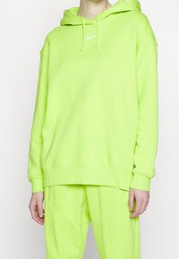 Neongrön huvtröja i mjukt tyg med en framtill liggande ficka, dragsko i huvan och en liten vit logotyp på bröstet. Matchas med matchandebyxor.