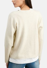 Pull crème à manches longues, col rond et détails d'ouverture latérale ; fabriqué en matériau doux et texturé.