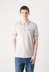 Polo cinza claro com detalhes pretos na gola e nas mangas, apresentando um pequeno logótipo preto "BOSS" no peito, feito de tecido respirável.