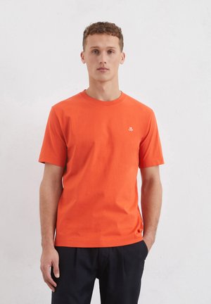 Oranges T-Shirt mit kurzen Ärmeln aus Baumwolle; verfügt über einen runden Halsausschnitt und ein kleines weißes Logo auf der linken Brustseite.