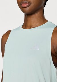 Αθλητικό αμάνικο τοπ σε ανοιχτό πράσινο μέντας με στρογγυλή λαιμόκοψη και αντανακλαστική λεπτομέρεια λογότυπου στο στήθος. Λείο, ελαστικό ύφασμα.