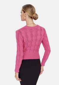 Maglione rosa a maglia con motivo a trecce, vita aderente e polsini e scollatura a costine, abbinato a una gonna nera. Vista posteriore.