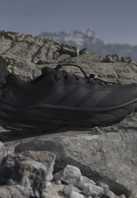 Chaussure de trail noire avec semelle Continental posée sur un terrain rocheux avec un arrière-plan de montagne flou.