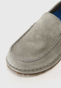 Gray suede loafers with a rounded toe, stitched detailing, and a rubber sole. The interior features a blue insole.