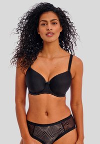 Sostén negro acolchado con textura acanalada, soporte de varilla y tirantes ajustables. Combinado con panties negros translúcidos que presentan un patrón de chevron.