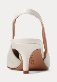 Bela usnjena slingback čevlja z visokim petom, videna iz zadnjega kota, s koničastim petom in rjavim podplatom, na katerem je delni prikaz logotipa.