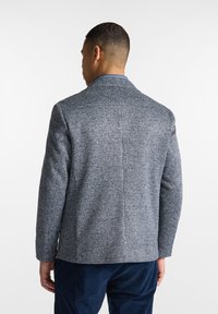 Blazer da uomo in tessuto intrecciato blu e grigio, con motivo a pied de poule, revers a punta e vestibilità sartoriale.