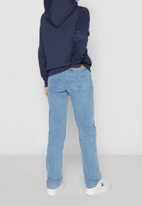 Vaqueros de mezclilla azul claro con corte recto, diseño de cinco bolsillos y costuras blancas. Combinados con una sudadera con capucha azul marino y zapatillas blancas.