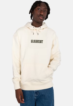 Cream-colored hoodie with a front pocket and drawstring hood. Features a green animal print logo on the chest. Worn with blue denim jeans.