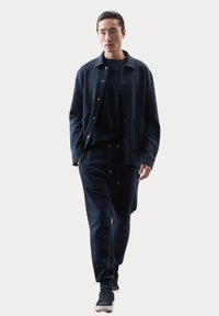 Completo in morbido tessuto blu navy, comprendente una giacca con bottoni e tasche e pantaloni abbinati, abbinato a sneaker scure. Design semplice e moderno.