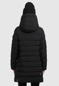 Crna softshell parka jakna, s kapuljačom, i rebrastim pletenim šeširom. Materijal je glatkog vrata s horizontalnim šavovima i bočnim patentnim zatvaračima.