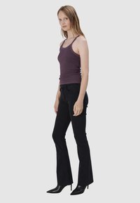 Donkere wassing flare jeans gecombineerd met een aansluitend paarse tanktop. Het model staat zijwaarts, waarbij het slanke silhouet en de elegante hoge hakken worden getoond.