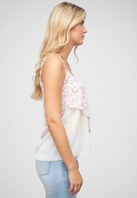 Ärmelloses Oberteil mit Blumenmuster und schicht design; darunter weißer Stoff. Helle Farben, weiche Textur, eng an den Armen, locker um die Taille.