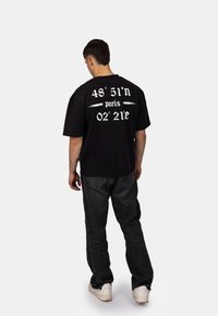 Černé tričko s krátkým rukávem a bílým textem, na zádech s vyznačenými souřadnicemi a nápisem "paris". V kombinaci s tmavě šedými džínami a bílými teniskami.