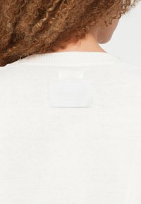 Λευκό πλεκτό πουλόβερ με ετικέτα στην πλάτη με ανάγλυφη την επιγραφή "REPLAY". Η υφή είναι απαλή με ριμπ λεπτομέρεια στο λαιμό.