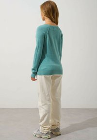Jersey turquesa de manga larga con puños acanalados, combinado con pantalones de corte relajado en color crema. Textura suave, diseño sin adornos.