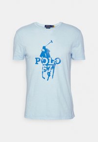 Světle modré bavlněné tričko s krátkým rukávem, které má modrou grafiku pólo hráče a odvážný nápis "POLO 67". Měkká textura, ležérní design.