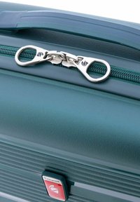 Maleta rígida color teal con un robusto cierre de cremallera con un mecanismo deslizante dual, logo de marca prominente y detalles en la superficie texturizados.