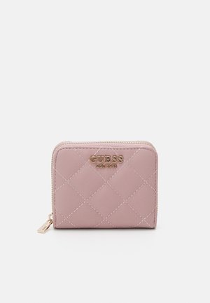 Petit portefeuille matelassé rose avec une fermeture éclair dorée et le logo "GUESS EST 1981" sur le devant, sur fond blanc.