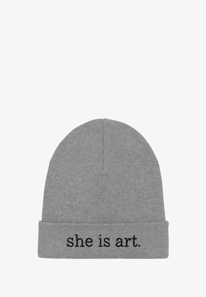 Bonnet gris en maille avec un revers arborant le texte « she is art. » en lettres noires. Texture douce, ajustement serré, design simple.
