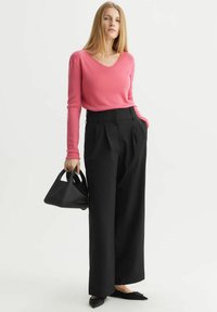Różowy sweter w serek, czarne szerokie spodnie, czarna torebka na ramię i czarne czółenka na szpic. Gładka faktura, elegancki design i dopasowany krój.