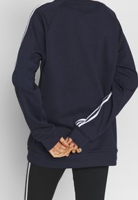 Sudadera azul marino con acentos de rayas blancas en las mangas, puños acanalados y dobladillo. Tejido suave con un corte relajado. Sin logotipos ni características visibles.