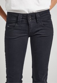 Svart jeans med smal passform, med dubbelknappning, framfickor och diskreta sömnadsdetaljer. Mjuk, texturerad tyg.