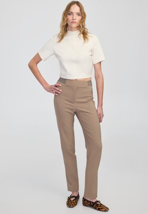 Krátký krémový top s krátkými rukávy, spárovaný s úzkými béžovými kalhotami a hnědými mokasínami se vzorem leopardí srsti. Hladké textury a neutrální barvy.