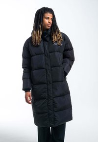 Cappotto imbottito nero con design lungo e forma squadrata, caratterizzato da un colletto alto, imbottitura spessa e polsini elastici. Logo sul petto.