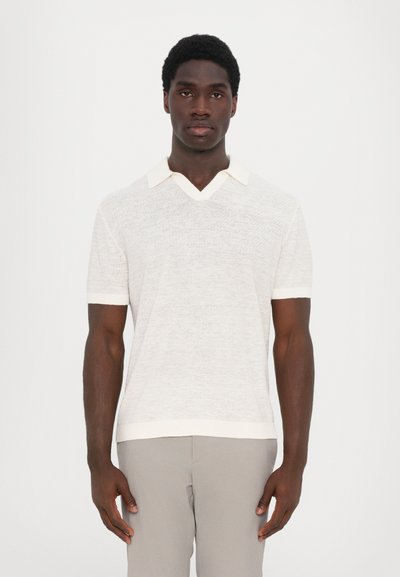 Polo a maniche corte di maglia beige chiaro con scollo a V, caratterizzato da colletto e polsini bianchi a contrasto, tessuto texture e vestibilità rilassata.