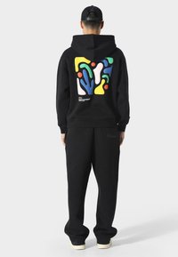 Sudadera negra con pantalones deportivos. La sudadera presenta un gráfico abstracto colorido en la parte posterior. Tejido suave, ajuste relajado, puños acanalados.