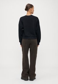 Sweatshirt preto com ombros caídos, punhos e bainha canelados. Combinado com calças largas castanhas com bolsos traseiros e uma textura suave.