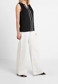 Haut noir sans manches avec un col en encoche et des bordures blanches, associé à un pantalon blanc à jambes larges et des sandales noires à bout ouvert.