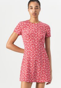 Robe florale rouge à manches courtes, décolleté rond, et un corsage ajusté qui s'évase à la taille. Motif de petites fleurs blanches et bleues sur l'ensemble.