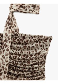 Beige kangas juu ambayo ina muonekano wa faru wa kahawia, ikiwa na mkanda uliokunjwa na texture iliyojaa. Muundo huu unasisitiza umbo lililo na muundo mzuri.