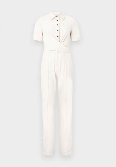 Λευκή ολόσωμη φόρμα με κοντά μανίκια, γιακά, μαύρα κουμπιά μπροστά, και λεπτομέρεια τύπου ζωνάκι στη μέση, παντελόνι με ίσια γραμμή.