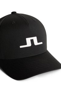 Svart keps gjord av slätter tyg med platt skärm. Har en upphöjd vit logotyp framtill och sömdetaljer längs skärmen.