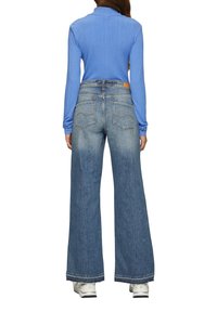 Lichtblauw geribbeld langemouwen top gecombineerd met wijde vervaagde blauwe jeans. De jeans hebben een leren label op de achterkant en zichtbare stiksels.