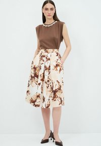 Top marrone senza maniche con un collo decorato, abbinato a una gonna svasata al ginocchio con stampa floreale nei toni crema e marrone.