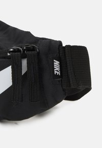 Svart nylon midjeväska med två dragkedjor, en avtagbar rem och ett vitt diagonalt streck. Har en liten Nike-logotagg.